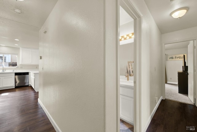 hallway with dark wood-type flooring, a textured wall, a sink, and baseboards