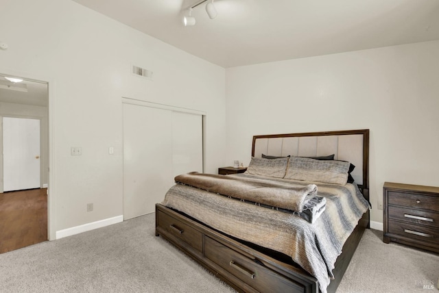 bedroom with light carpet, baseboards, visible vents, rail lighting, and a closet