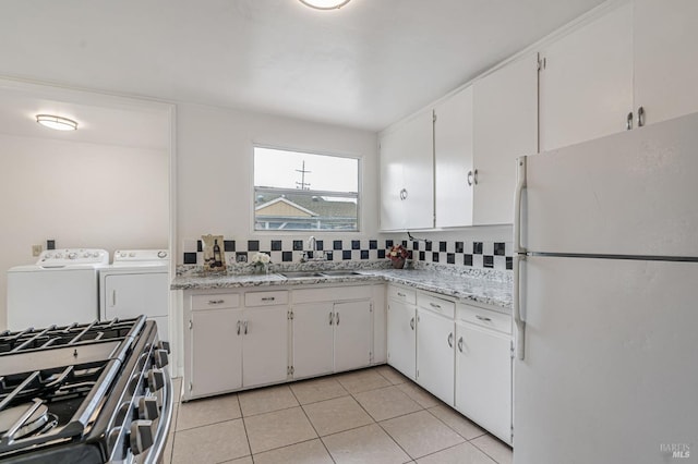 kitchen featuring freestanding refrigerator, stainless steel gas stove, a sink, white cabinetry, and washer and dryer