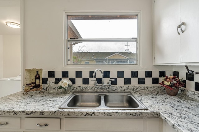 kitchen with tasteful backsplash, washer / clothes dryer, a sink, and white cabinetry