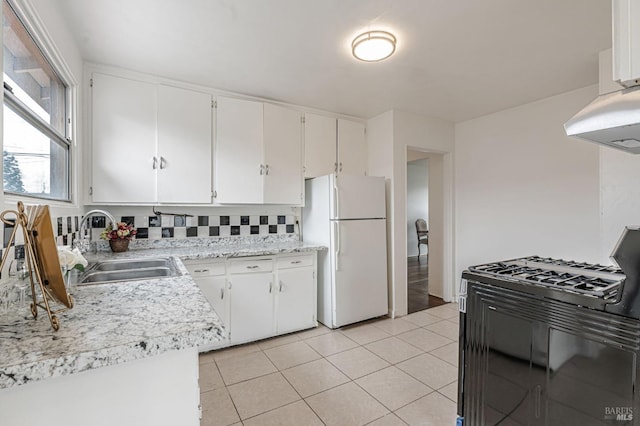 kitchen with light tile patterned floors, light countertops, freestanding refrigerator, black gas stove, and a sink