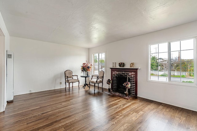 sitting room with a textured ceiling, a brick fireplace, wood finished floors, and baseboards