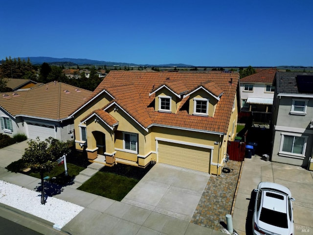 view of front facade featuring a mountain view, a tiled roof, a garage, stucco siding, and driveway