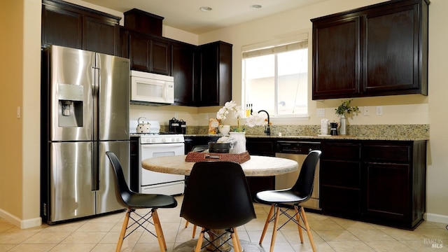 kitchen with dark brown cabinetry, light tile patterned flooring, a sink, stainless steel appliances, and baseboards