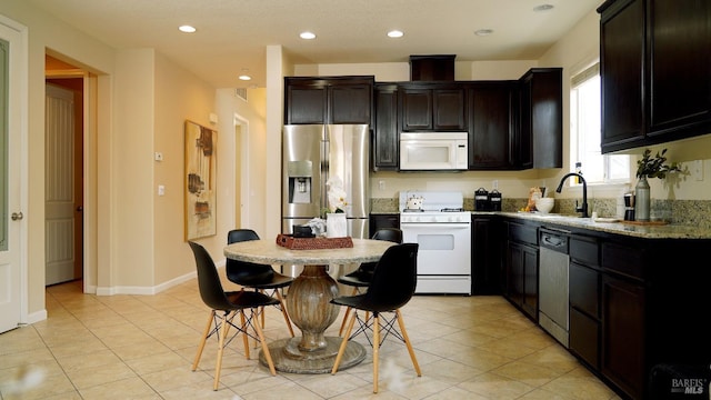 kitchen with light tile patterned floors, recessed lighting, appliances with stainless steel finishes, light stone counters, and a sink
