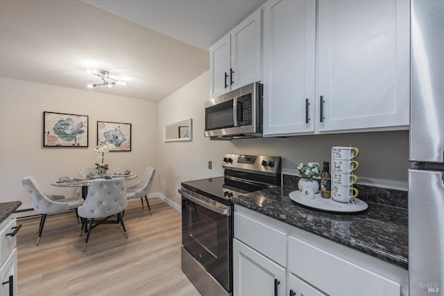 kitchen with light wood-style flooring, white cabinetry, stainless steel appliances, and dark stone counters