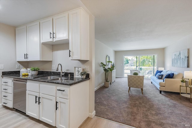 kitchen featuring a sink, white cabinets, open floor plan, stainless steel dishwasher, and dark stone countertops