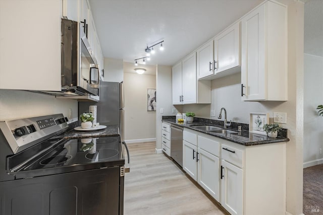 kitchen with a sink, white cabinetry, appliances with stainless steel finishes, light wood-type flooring, and dark stone countertops