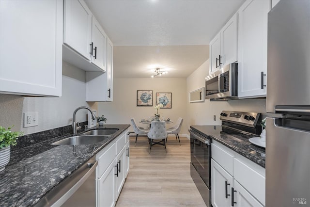 kitchen featuring stainless steel appliances, dark stone counters, white cabinets, and a sink