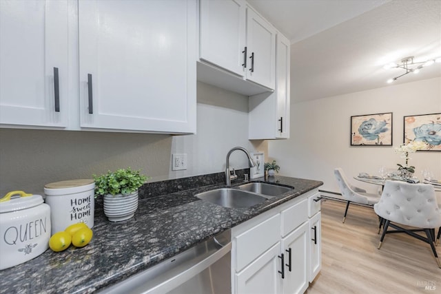 kitchen featuring light wood-style floors, white cabinetry, a sink, and dark stone countertops