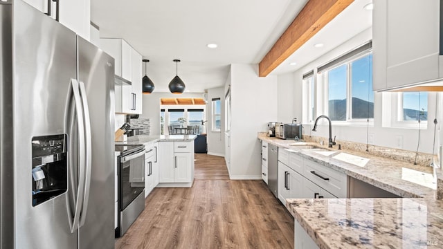 kitchen with light stone counters, stainless steel appliances, hanging light fixtures, white cabinetry, and a sink