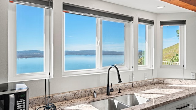 kitchen with light stone counters, a water view, and a sink