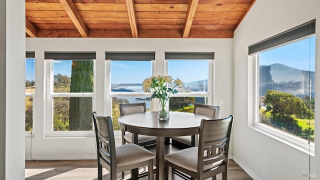 dining room with baseboards, lofted ceiling with beams, wooden ceiling, wood finished floors, and a water and mountain view