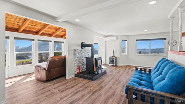 living room with light wood finished floors, baseboards, lofted ceiling with beams, a wall mounted air conditioner, and a wood stove