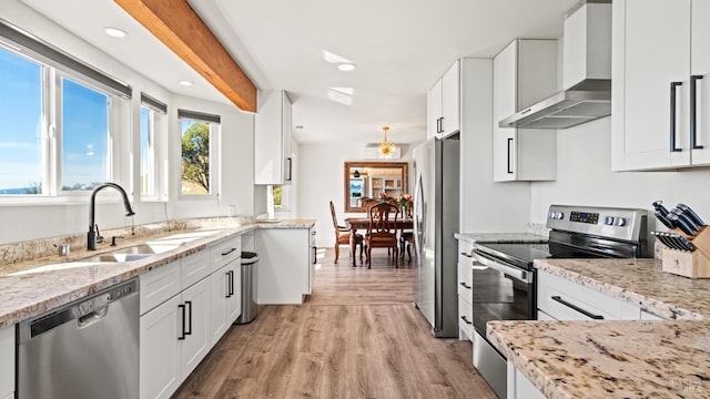 kitchen featuring wall chimney range hood, appliances with stainless steel finishes, white cabinets, and a sink