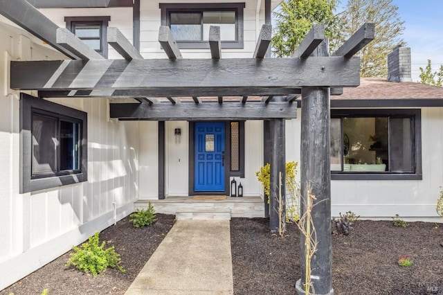 entrance to property with a shingled roof and a pergola