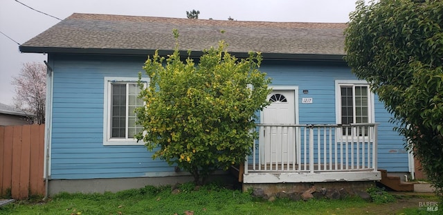 view of front facade with covered porch, a shingled roof, and fence