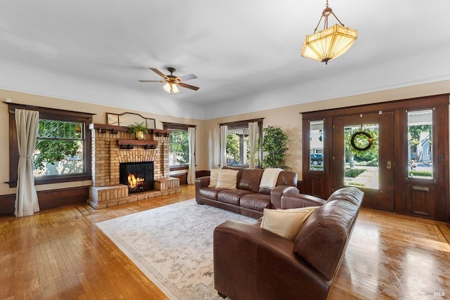 living room with light wood-style floors, a brick fireplace, plenty of natural light, and a ceiling fan