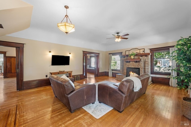 living room with a brick fireplace, plenty of natural light, light wood-style flooring, and baseboards