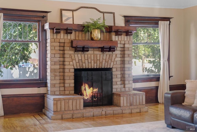 living area featuring a healthy amount of sunlight, a fireplace, ornamental molding, and wood finished floors