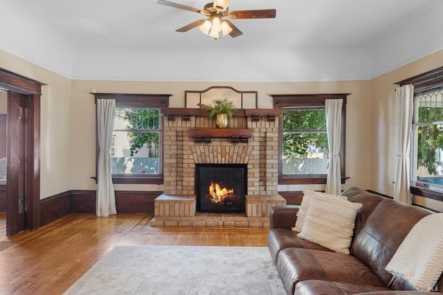 living area with a healthy amount of sunlight, a fireplace, light wood-style flooring, and ceiling fan