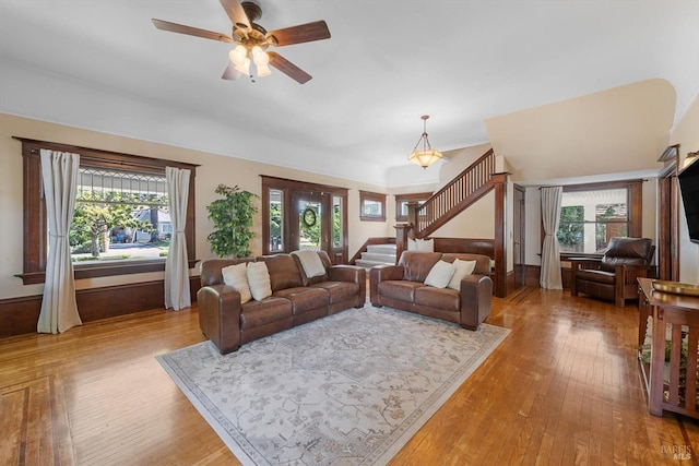 living area with stairway, plenty of natural light, wood finished floors, and a ceiling fan