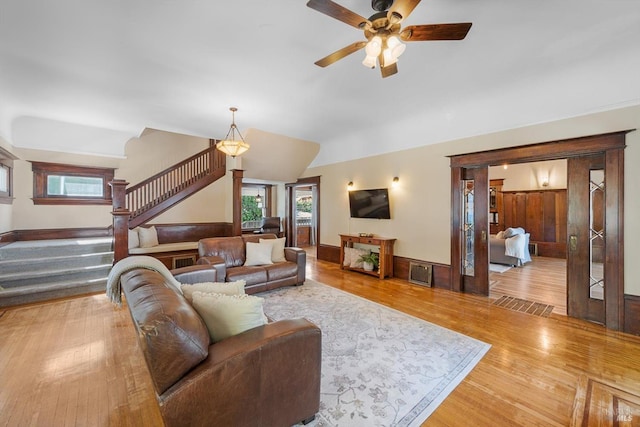 living area with lofted ceiling, a ceiling fan, baseboards, stairs, and light wood-style floors