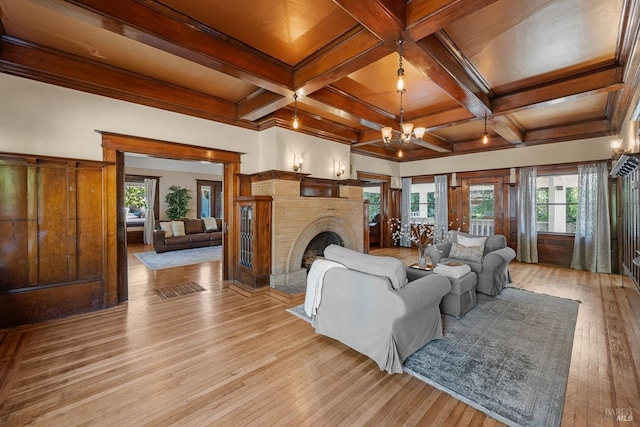 living room with a notable chandelier, light wood finished floors, a fireplace with raised hearth, coffered ceiling, and beamed ceiling