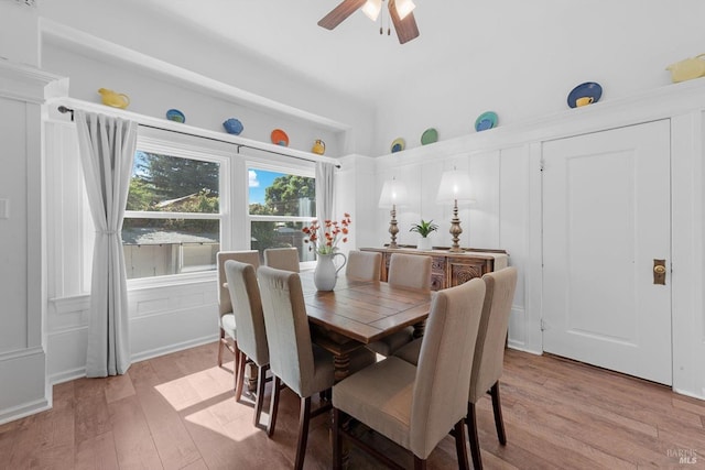 dining area featuring light wood-style floors, a decorative wall, and a ceiling fan