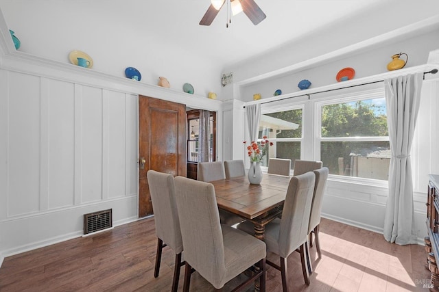 dining space featuring ceiling fan, visible vents, a decorative wall, and wood finished floors