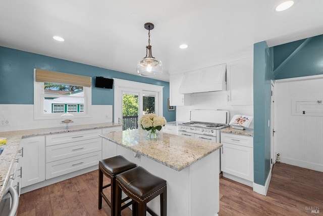 kitchen featuring premium range hood, a kitchen island, white cabinetry, hanging light fixtures, and white gas range