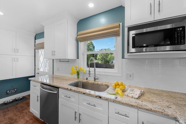 kitchen with a sink, white cabinetry, a healthy amount of sunlight, appliances with stainless steel finishes, and light stone countertops