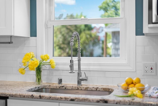 room details with light stone counters, white cabinetry, a sink, and decorative backsplash