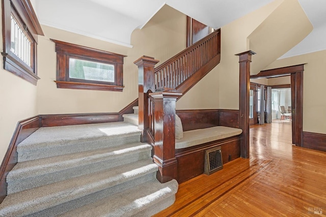 stairs with ornate columns, wood finished floors, and wainscoting