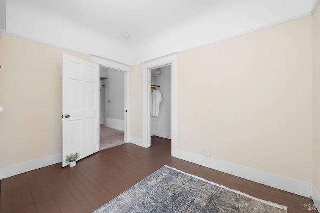 unfurnished bedroom featuring dark wood-style floors, a walk in closet, a closet, and baseboards