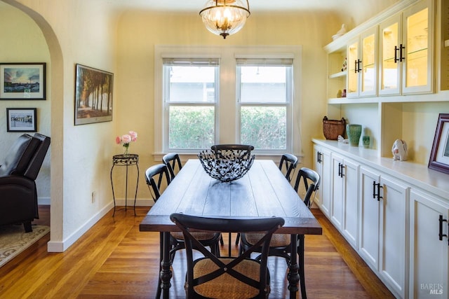 dining room with arched walkways, baseboards, and light wood finished floors