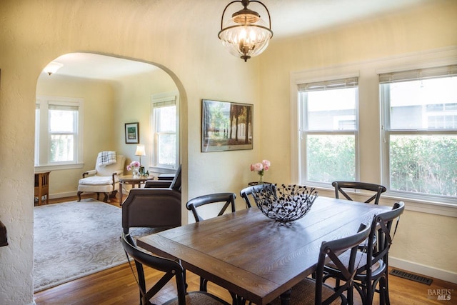 dining area featuring baseboards, visible vents, arched walkways, and wood finished floors