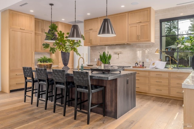 kitchen with light wood-type flooring, light brown cabinets, and an island with sink