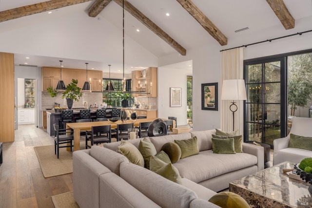 living area featuring visible vents, an inviting chandelier, light wood-style floors, high vaulted ceiling, and beamed ceiling