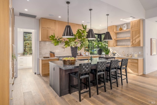 kitchen featuring visible vents, a sink, a center island with sink, and light brown cabinetry