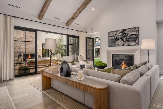 living room featuring beam ceiling, visible vents, light wood-style flooring, a glass covered fireplace, and high vaulted ceiling