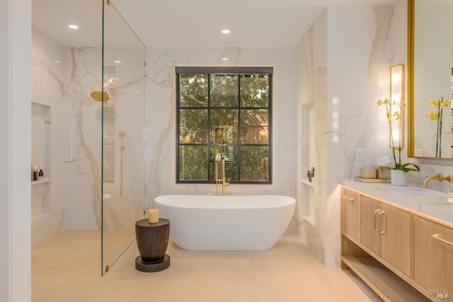 full bathroom featuring tile walls, recessed lighting, a soaking tub, vanity, and stone wall