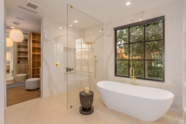 bathroom featuring a marble finish shower, a freestanding tub, stone wall, tile walls, and recessed lighting