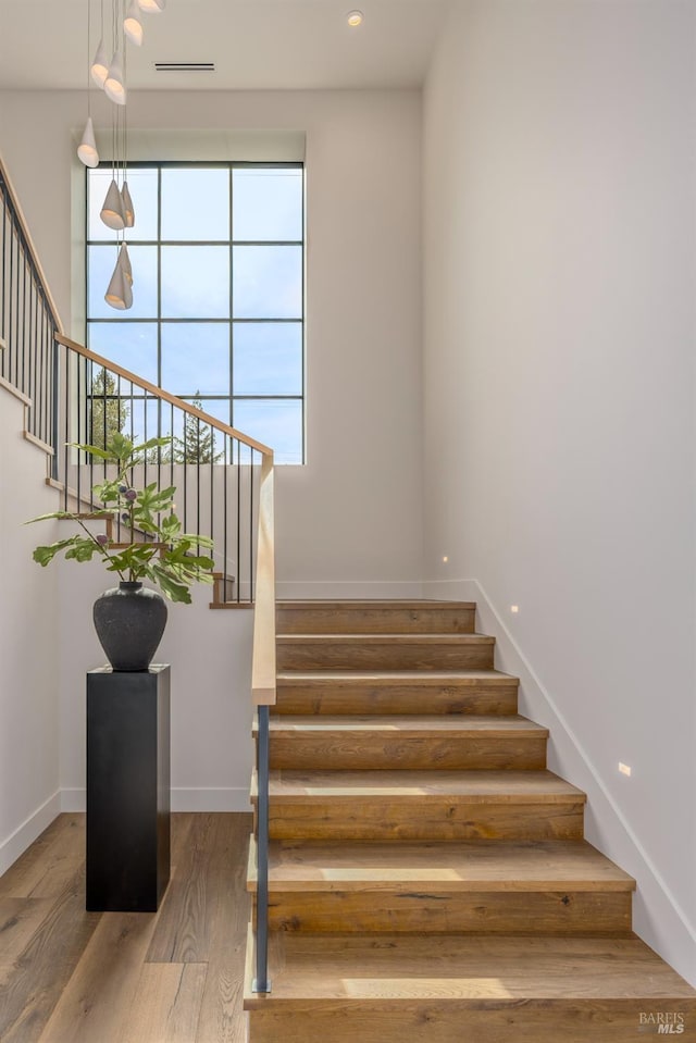 stairway featuring wood finished floors, visible vents, and baseboards