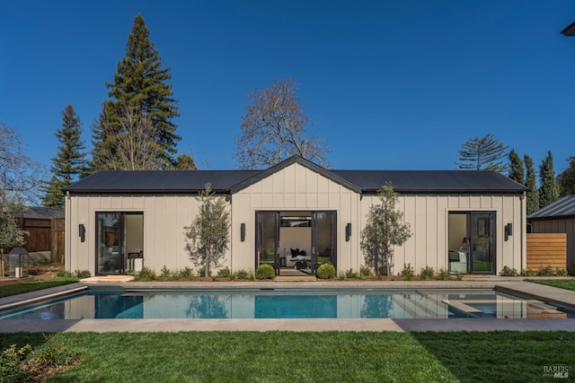 rear view of property with board and batten siding, an outdoor pool, a yard, and fence