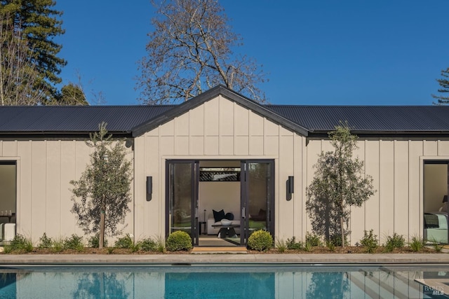 back of house featuring board and batten siding, an outdoor pool, and metal roof