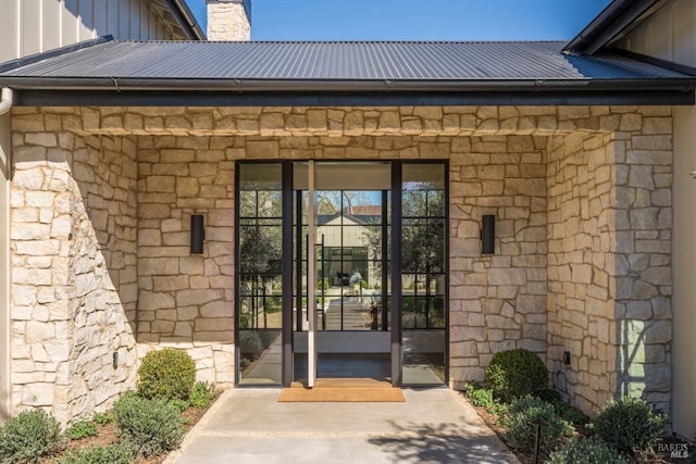 property entrance featuring board and batten siding, stone siding, and metal roof