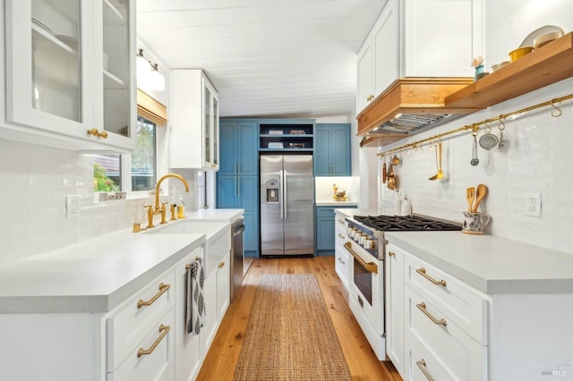 kitchen featuring blue cabinets, light countertops, appliances with stainless steel finishes, light wood-type flooring, and open shelves