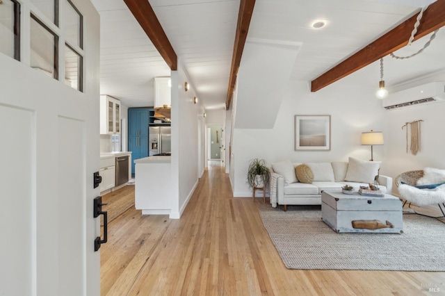 living room with beam ceiling, a wall unit AC, baseboards, and light wood finished floors