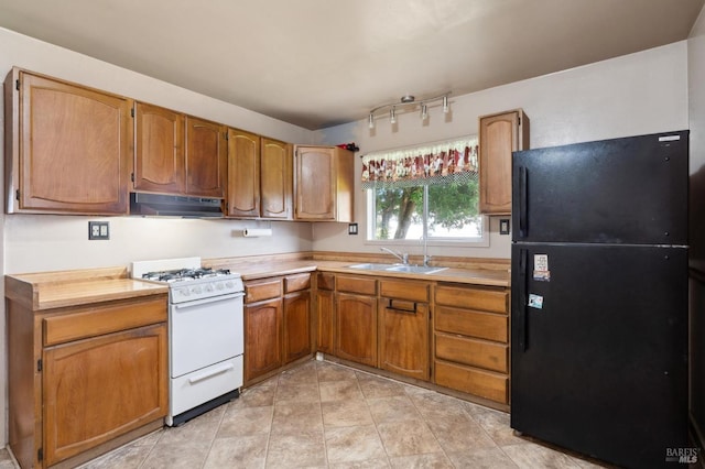 kitchen with light countertops, freestanding refrigerator, a sink, under cabinet range hood, and white gas range oven